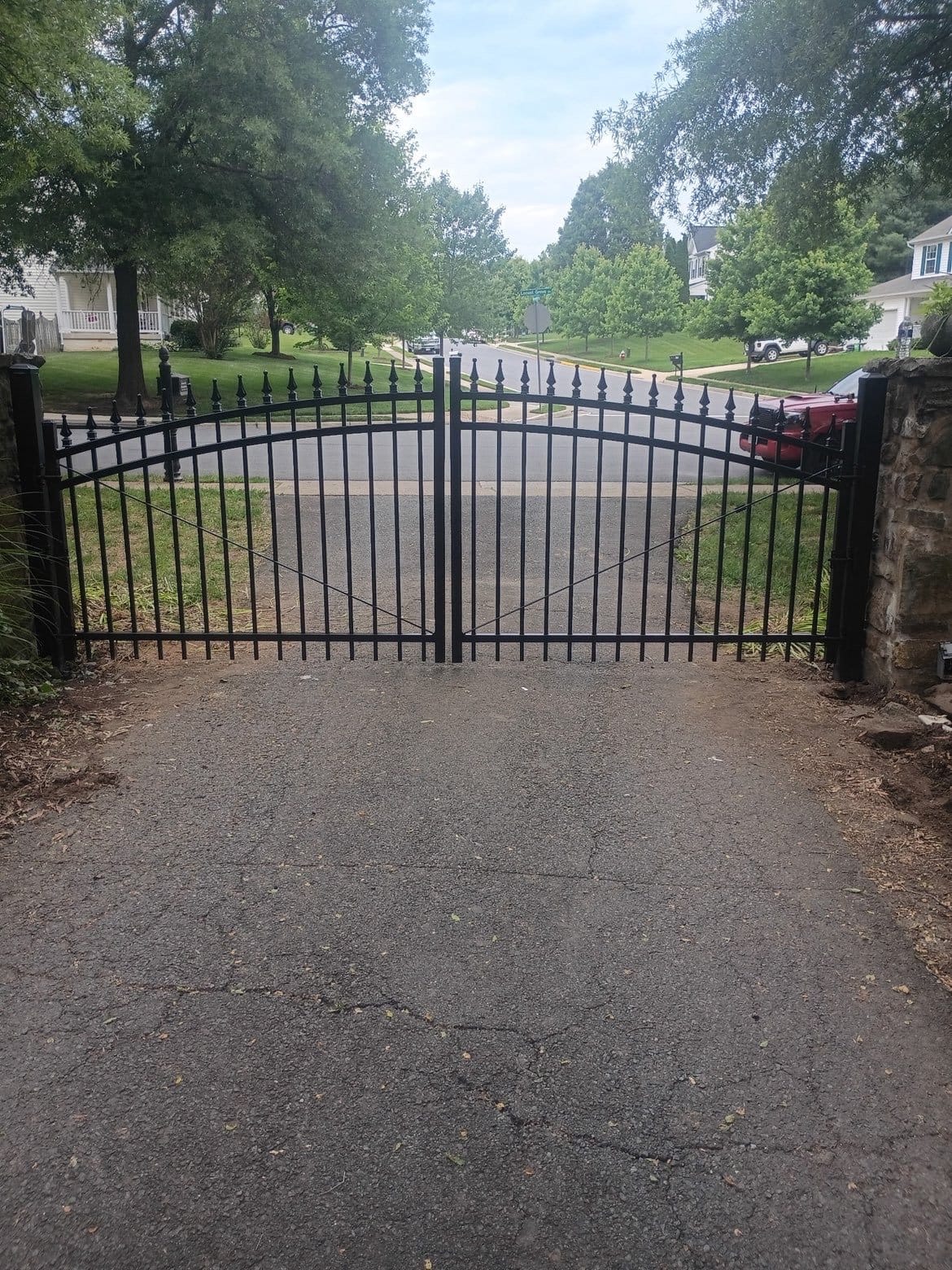 Arched black aluminum double entry gate on stone piers at the head of a driveway