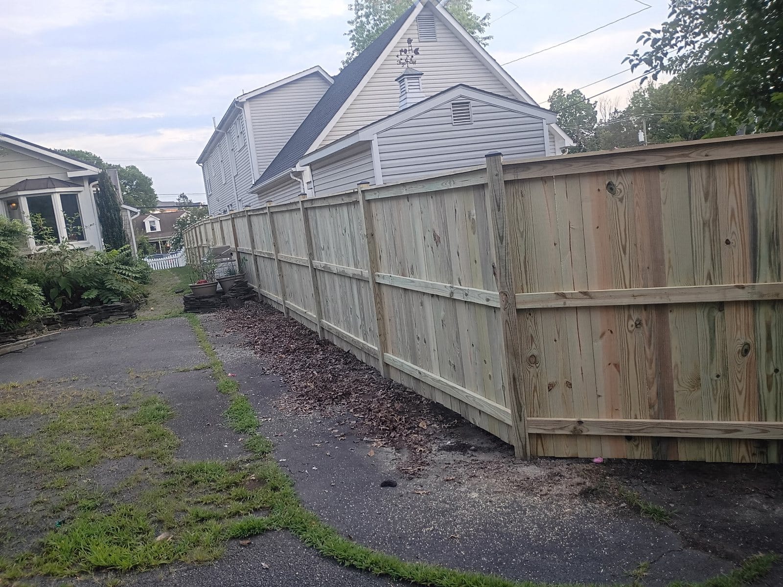 Pressure treated wood privacy fence running the length of a shared driveway
